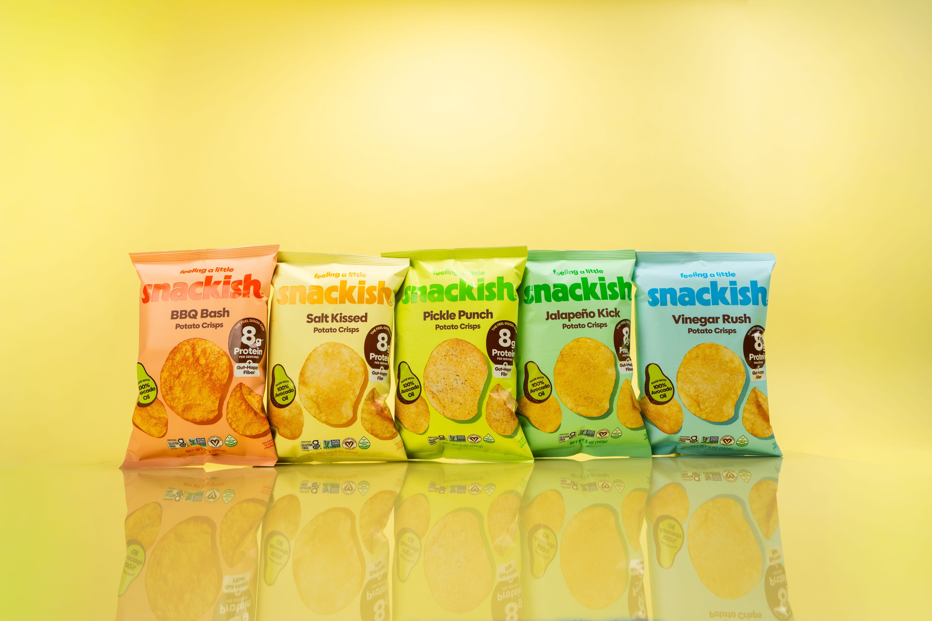Five colourful bags of Snackish potato crisps arranged on a reflective yellow set.