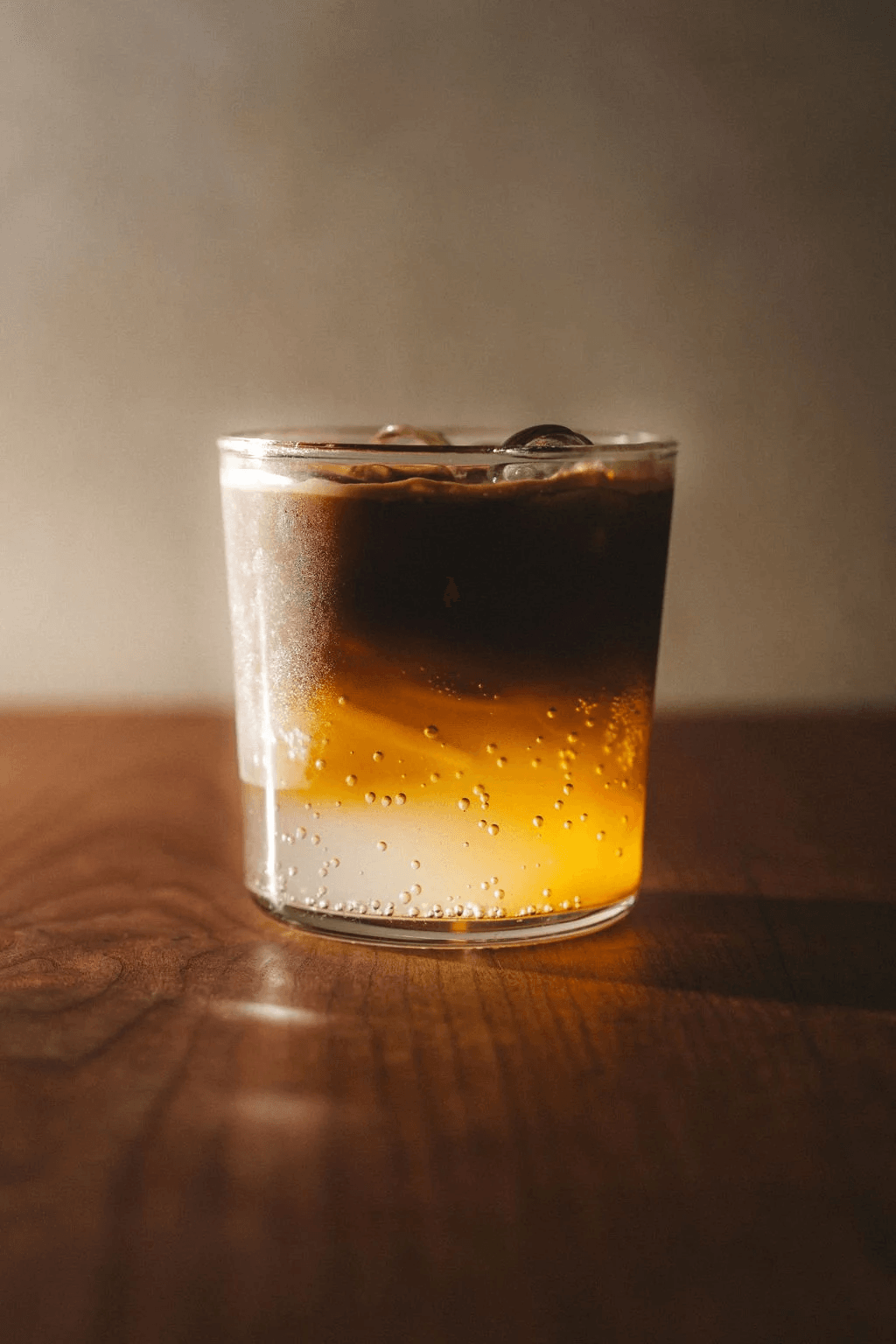 An amber iced coffee in a low glass on a wooden table.