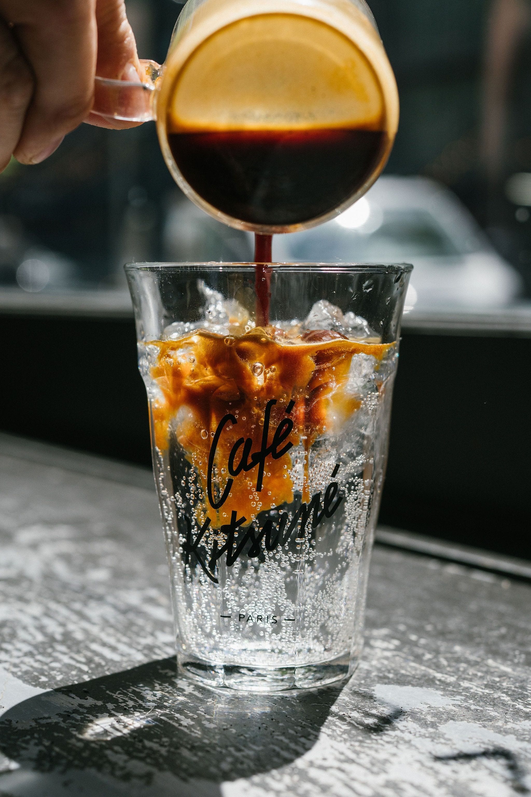 Espresso poured over ice into a Café Kitsuné glass on a sunlit countertop.